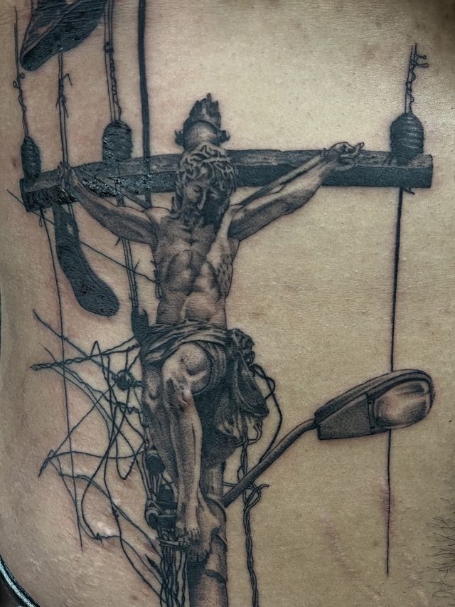 Black and grey crucifixion scene with the cross drawn as a power pole tangled in lines, on a back.