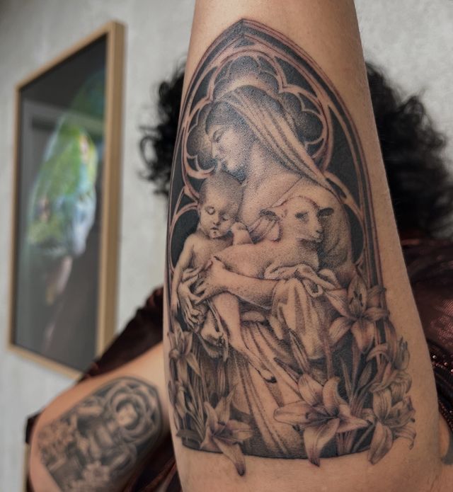 Madonna holding a child and a lamb inside a gothic arch framed by lilies, on an upper arm.