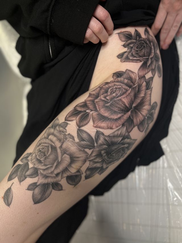 Cluster of black and grey roses across the outer thigh.