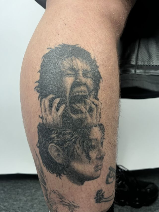 Surreal black and grey calf piece — a screaming face lifted open like a lid above a woman's calm profile.