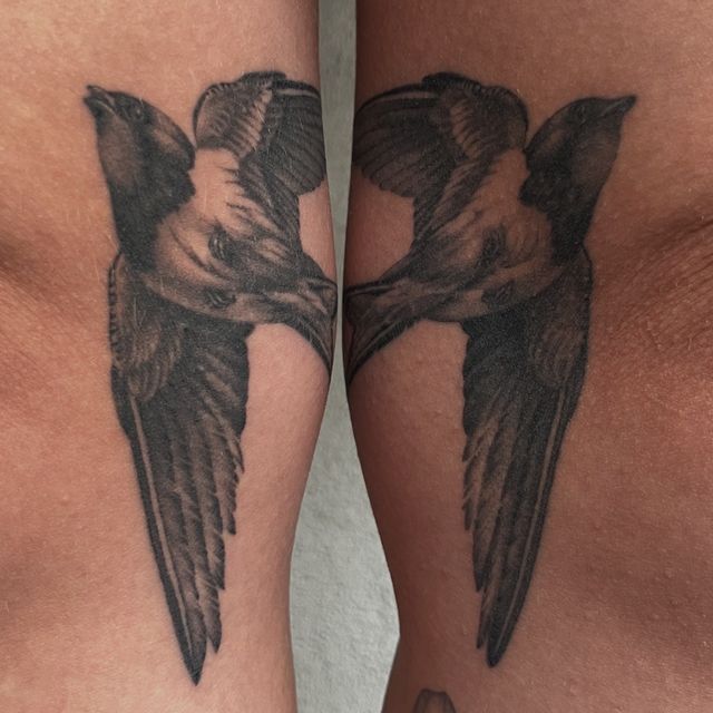 Matching black and grey swallows in flight, one on each forearm.