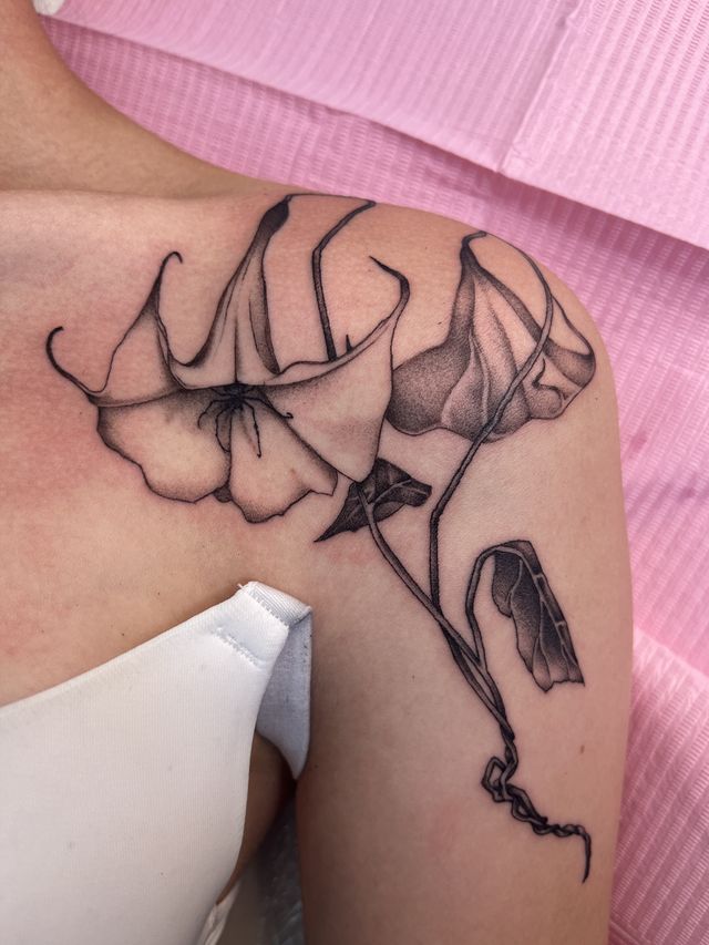 Fine line trumpet flowers and leaves along the collarbone and shoulder.