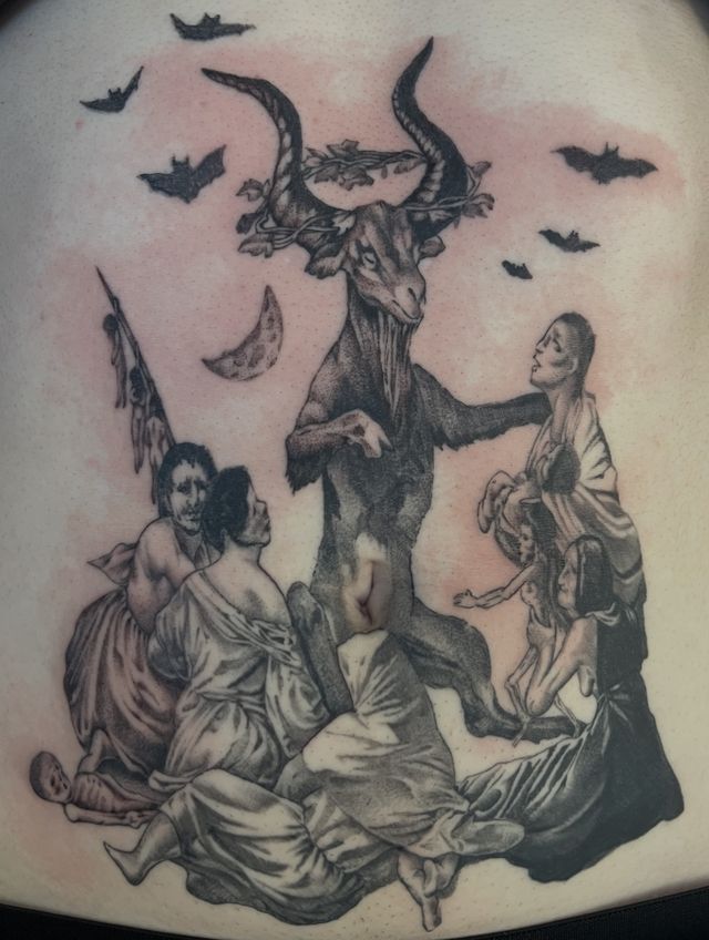 Black and grey witches' sabbath scene on a lower back — a horned goat surrounded by robed figures and bats.